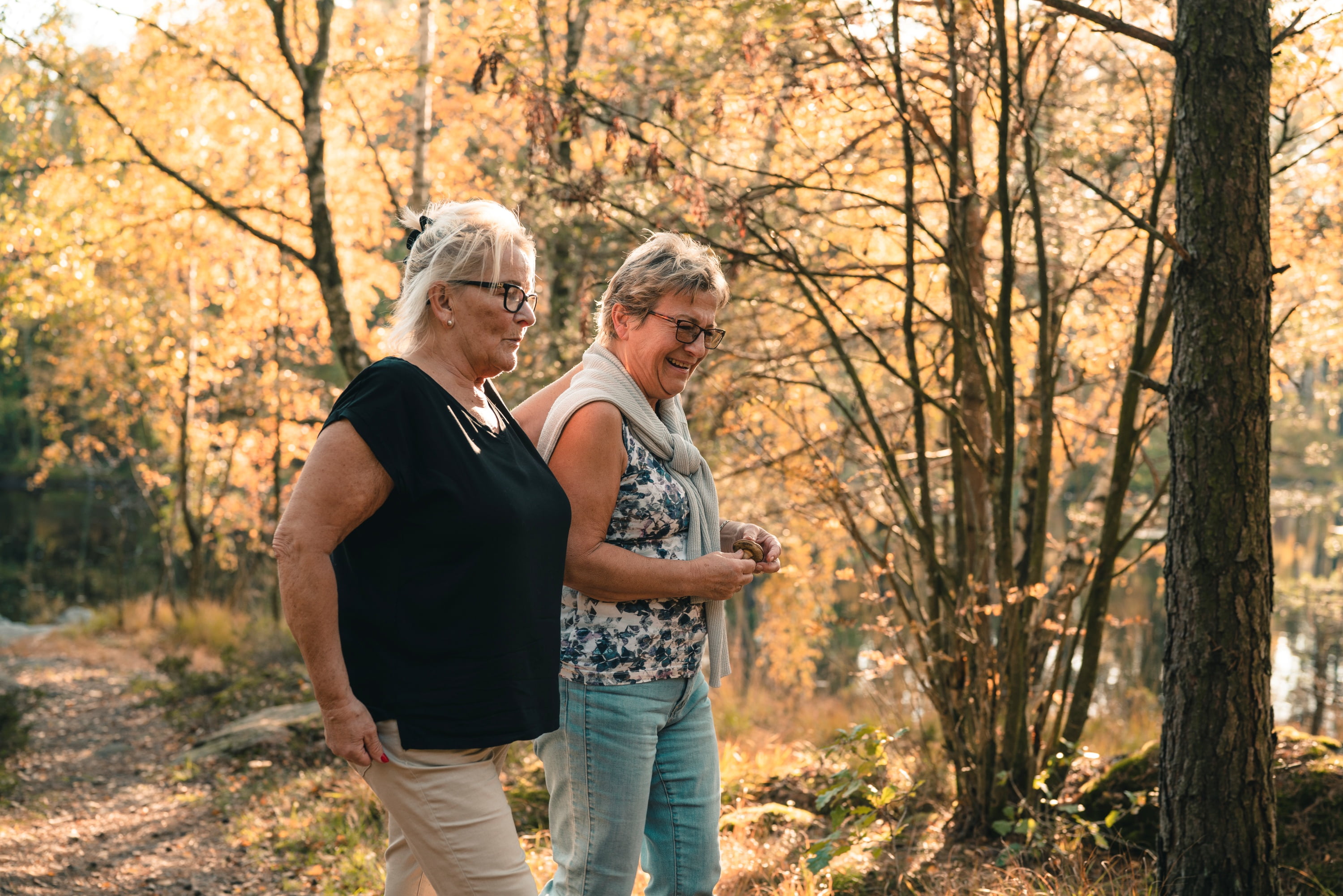 To litt eldre kvinner går på tur i skogen en varm høstdag.
