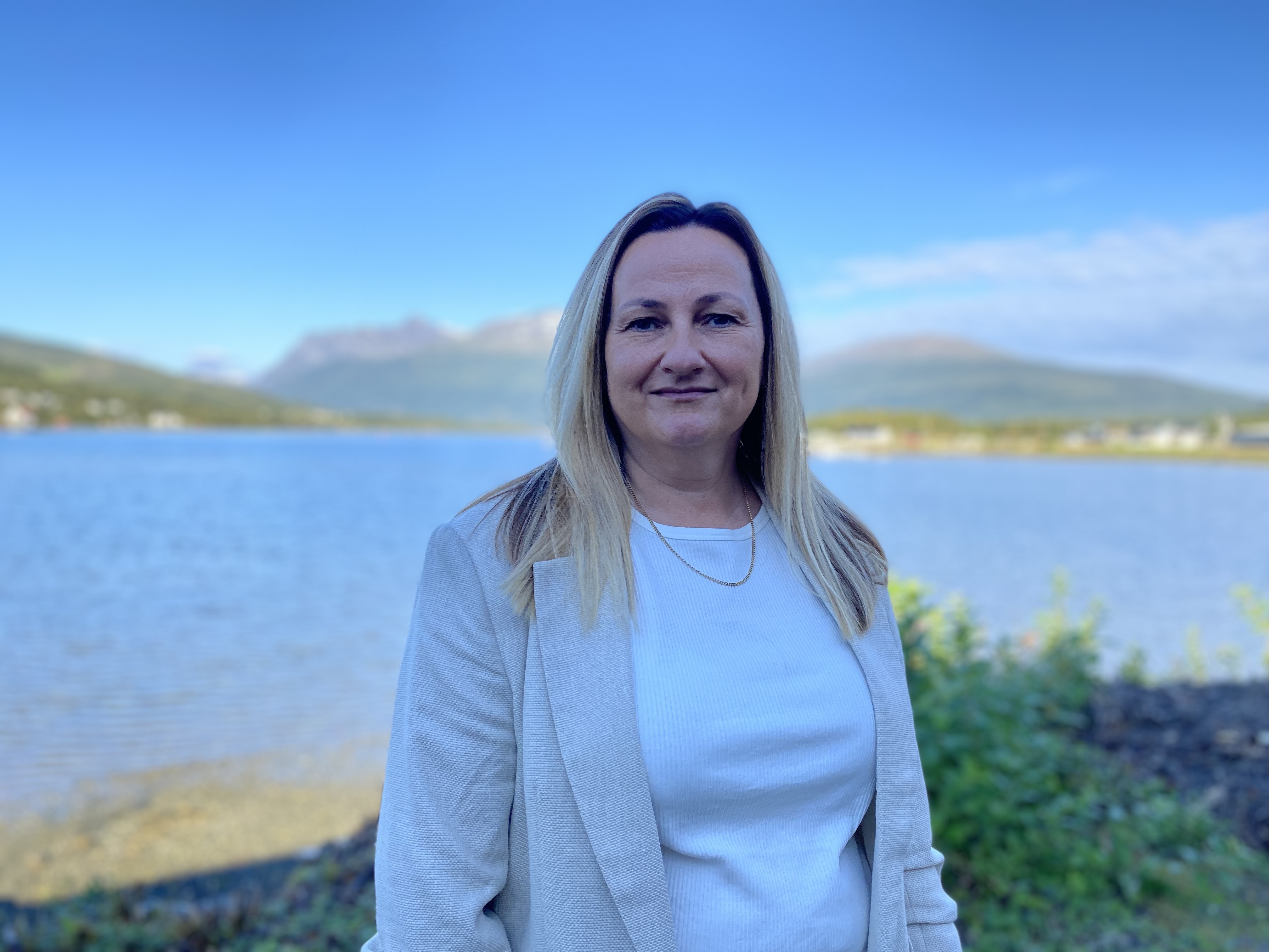 Bedriftsleder May Britt Flatmo står med havet og fjellet i bakgrunnen en vakker sommerdag