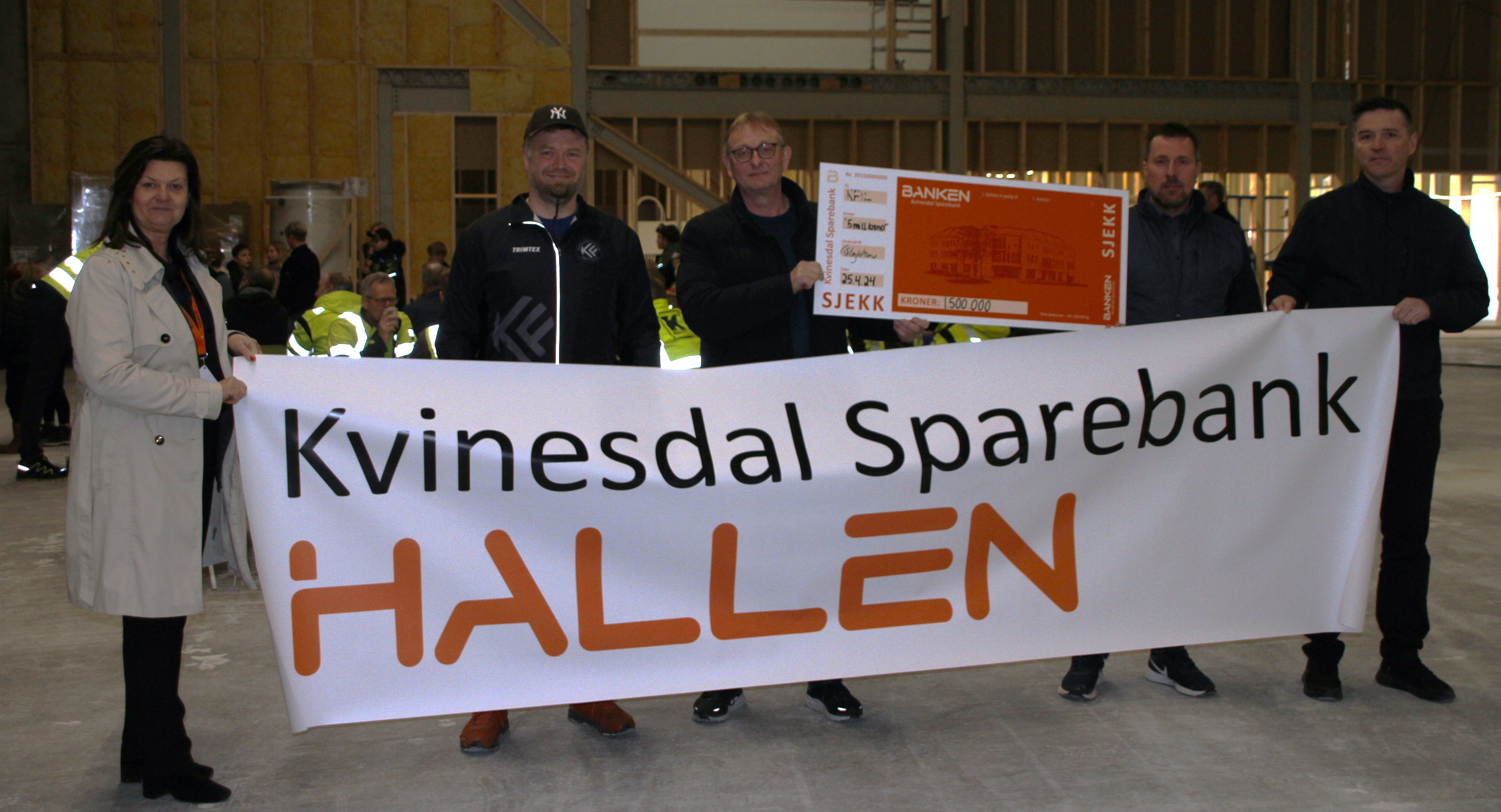 Administrerende banksjef Tone Egeland Syvertsen holder en stor banner med navnet: Kvinesdal Sparebank HALLEN sammen med andre under utdelingen av en sjekk på 1,5 millioner kroner.