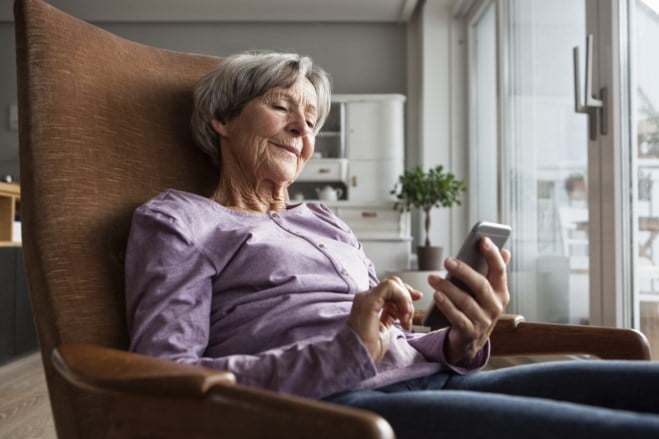 Eldre dame med lilla genser som ser på mobil